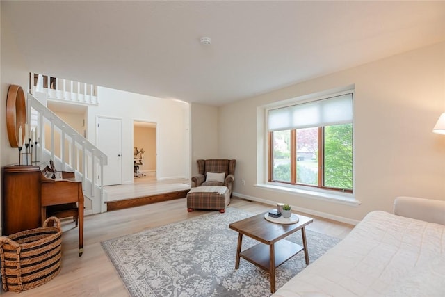 living area with light wood-type flooring, stairs, and baseboards