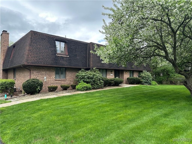 view of front of house featuring roof with shingles, mansard roof, brick siding, a front lawn, and a chimney