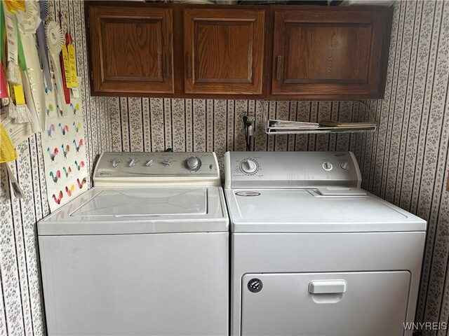 washroom with wallpapered walls, cabinet space, and washer and clothes dryer