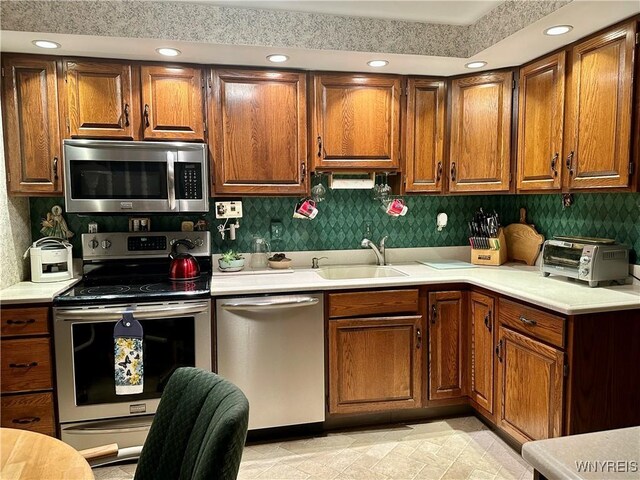 kitchen featuring stainless steel appliances, a sink, light countertops, brown cabinetry, and recessed lighting