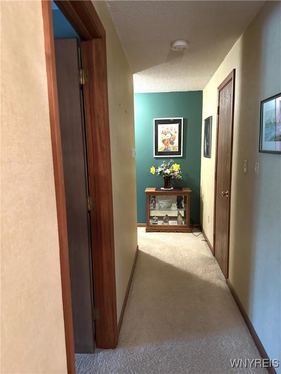 hallway featuring carpet floors, a textured ceiling, and baseboards