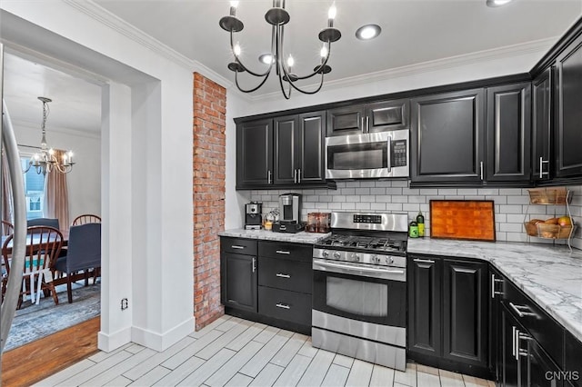 kitchen with appliances with stainless steel finishes, a chandelier, dark cabinetry, and ornamental molding