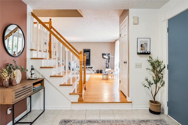 entrance foyer featuring stairs, tile patterned floors, healthy amount of natural light, a textured ceiling, and baseboards