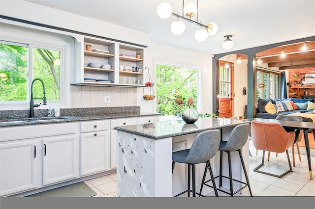 kitchen featuring a sink, arched walkways, light tile patterned floors, a kitchen bar, and dark stone counters