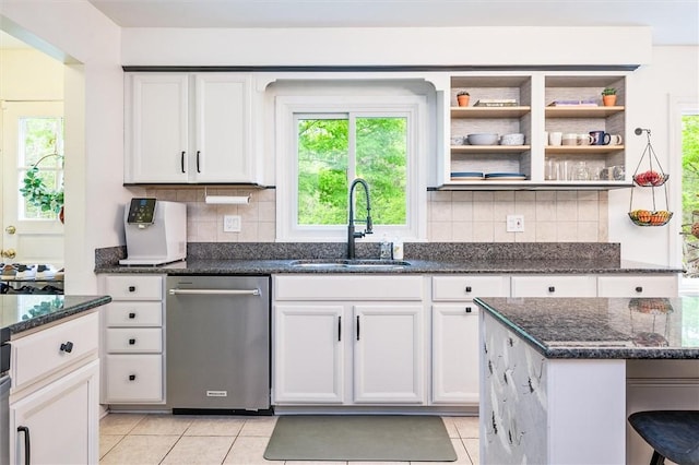 kitchen with dishwasher, a sink, light tile patterned flooring, and dark stone countertops