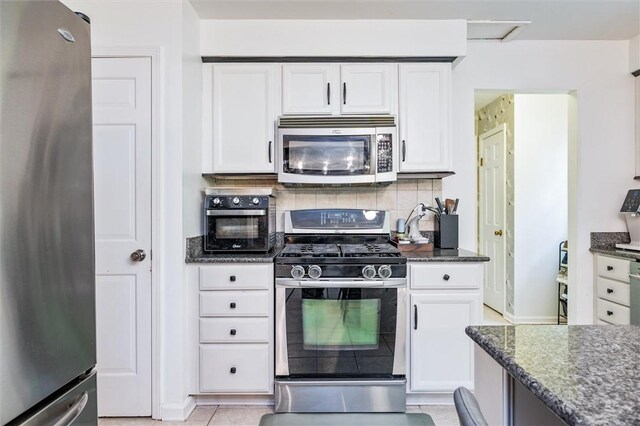 kitchen featuring stainless steel appliances, white cabinets, decorative backsplash, dark stone countertops, and light tile patterned floors