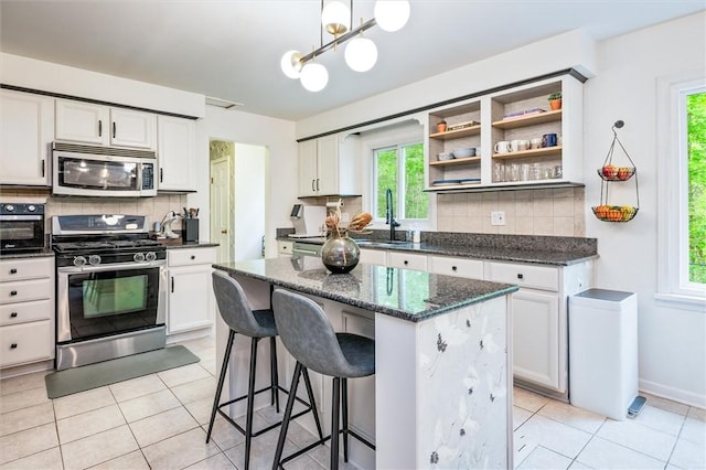 kitchen with appliances with stainless steel finishes, a sink, backsplash, a center island, and white cabinets