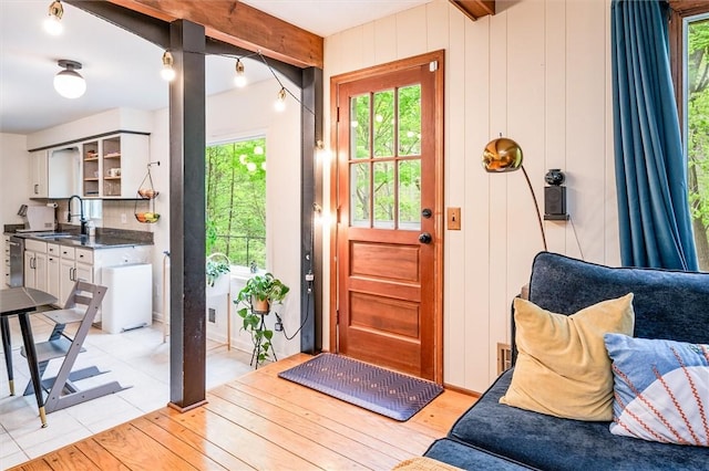 doorway featuring a sink, beamed ceiling, and light wood-style floors