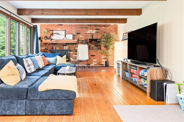 living room with hardwood / wood-style floors, beamed ceiling, a fireplace, and brick wall