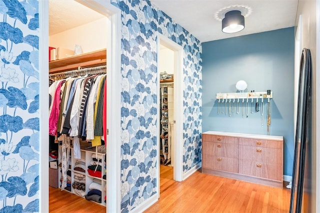 bedroom featuring light wood finished floors, wallpapered walls, baseboards, and a closet