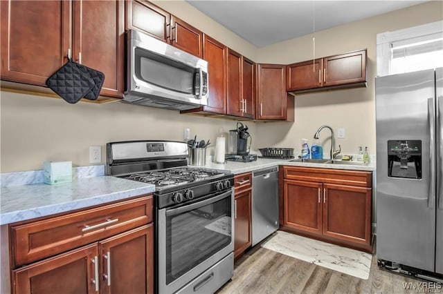 kitchen with stainless steel appliances, a sink, light wood finished floors, and light stone countertops