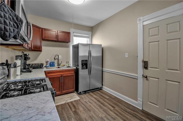 kitchen with appliances with stainless steel finishes, a sink, light countertops, wood finished floors, and baseboards