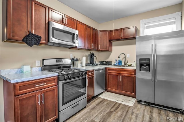 kitchen featuring appliances with stainless steel finishes, a sink, light wood-style floors, and light stone counters