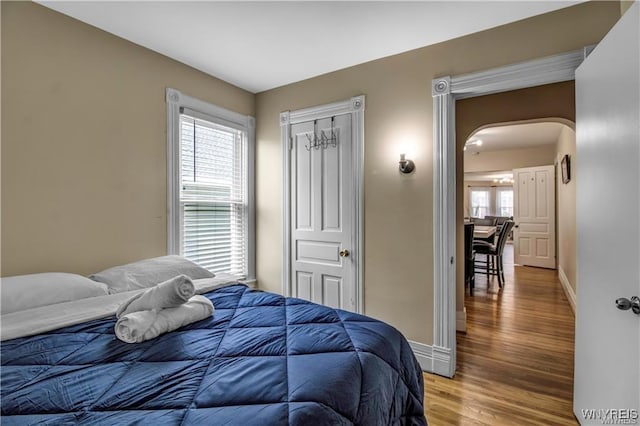 bedroom featuring baseboards, light wood-style floors, and arched walkways
