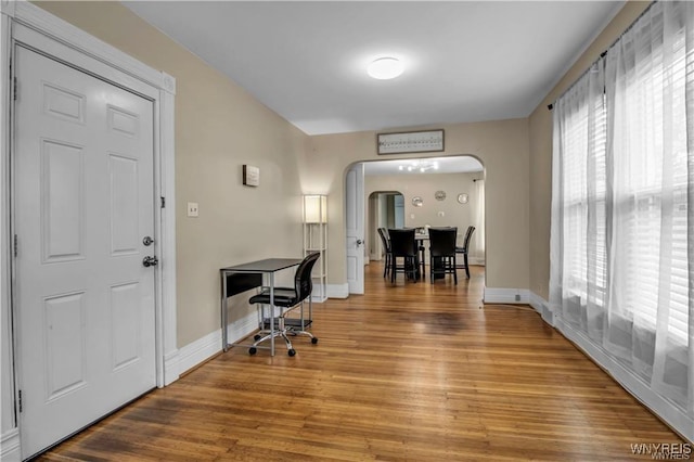 foyer featuring arched walkways, light wood-type flooring, and baseboards