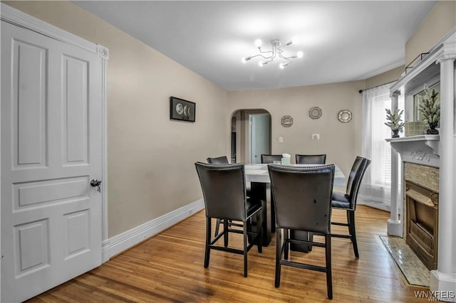 dining space featuring arched walkways, wood finished floors, a fireplace with flush hearth, and baseboards