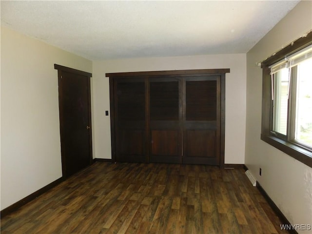 unfurnished bedroom with dark wood-style floors, baseboards, and a closet