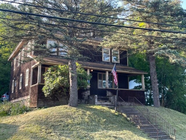view of front of home with stairs, covered porch, and a front lawn