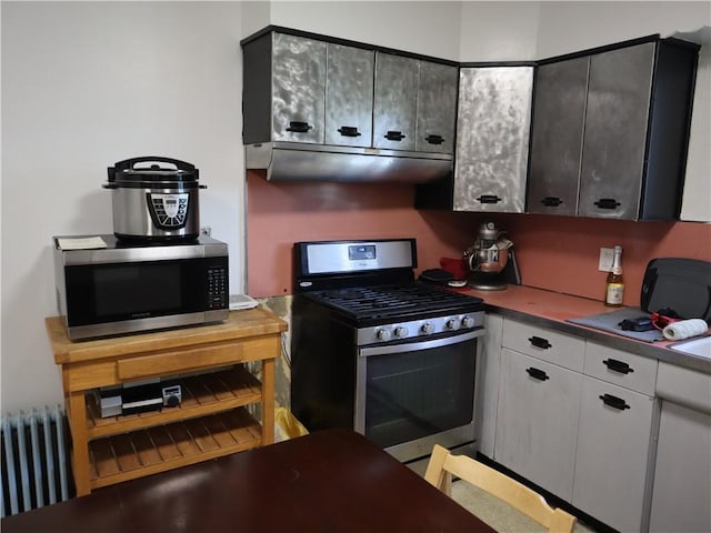 kitchen featuring stainless steel appliances, radiator heating unit, under cabinet range hood, white cabinets, and dark countertops