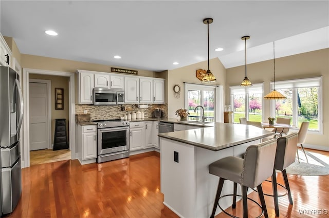 kitchen featuring stainless steel appliances, a peninsula, white cabinetry, wood finished floors, and lofted ceiling