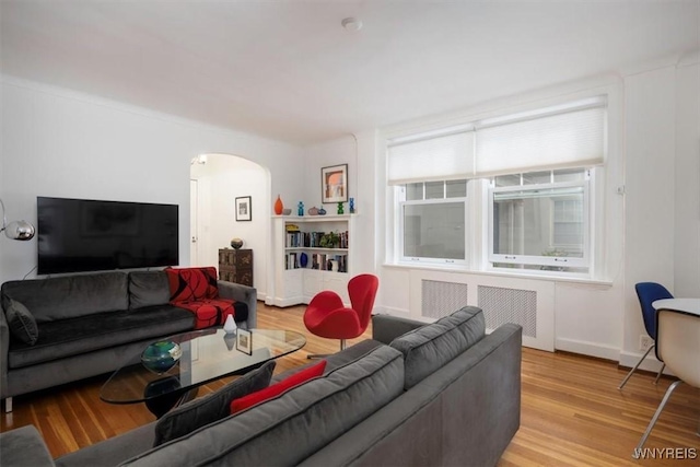 living room with arched walkways, light wood-style flooring, and baseboards