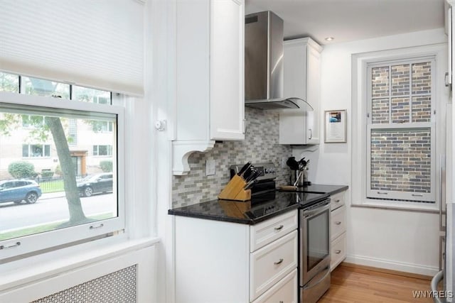 kitchen with wall chimney range hood, stainless steel electric range oven, decorative backsplash, and white cabinetry