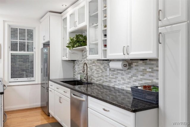 kitchen with a sink, appliances with stainless steel finishes, white cabinets, backsplash, and light wood-style floors