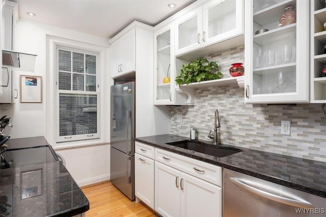 kitchen featuring appliances with stainless steel finishes, a sink, white cabinets, light wood-style flooring, and dark stone counters