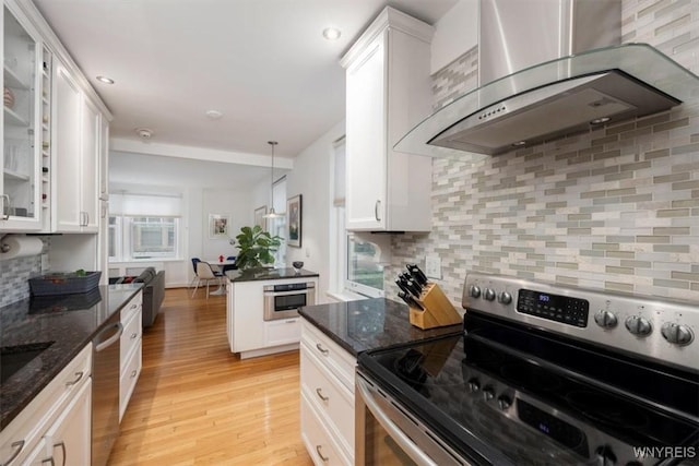 kitchen featuring appliances with stainless steel finishes, wall chimney range hood, white cabinetry, and light wood finished floors