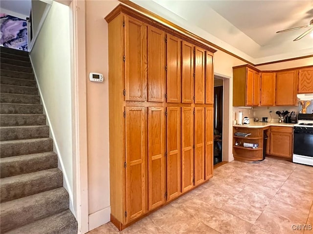 237 James St, Lenox, NY 13032 - kitchen with white gas stove, ceiling fan, brown cabinets, under cabinet range hood, and light countertops