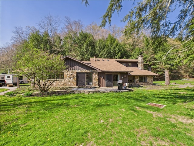 back of property with board and batten siding, a chimney, a lawn, and stone siding