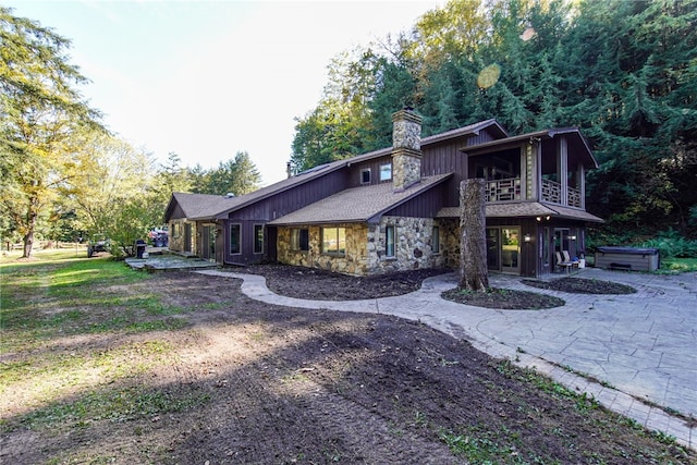 view of front of property featuring stone siding, a chimney, a balcony, and a patio