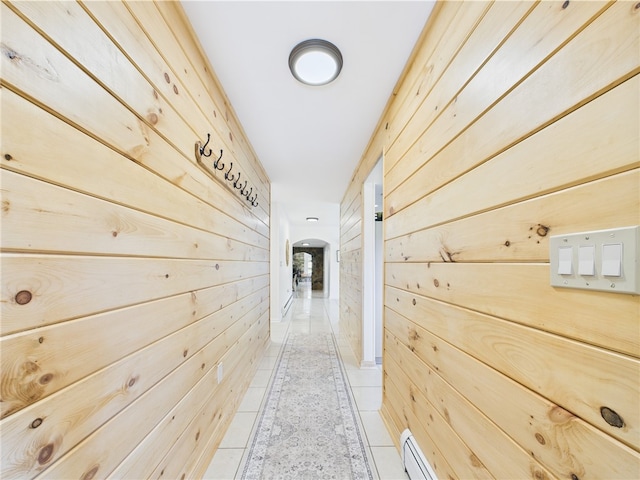hallway featuring wooden walls, arched walkways, light tile patterned floors, and a baseboard heating unit