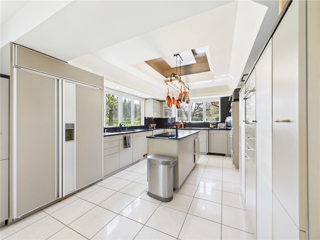 kitchen with a raised ceiling, paneled refrigerator, a kitchen island, dark countertops, and a chandelier