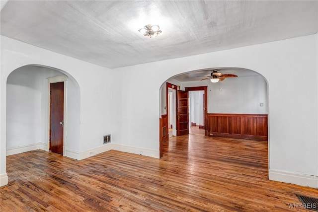 spare room with a ceiling fan, wood finished floors, arched walkways, and baseboards