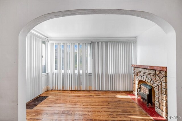 unfurnished living room with wood finished floors, arched walkways, and a stone fireplace