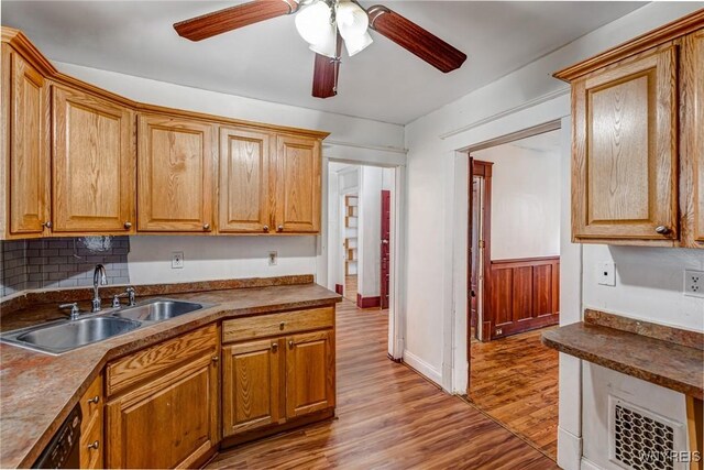 kitchen featuring a sink, light wood finished floors, black dishwasher, a ceiling fan, and dark countertops