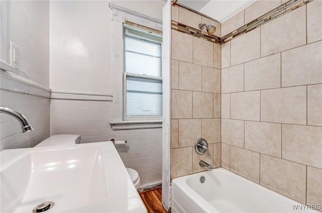 bathroom with tile walls, toilet, a sink, shower / tub combination, and wood finished floors