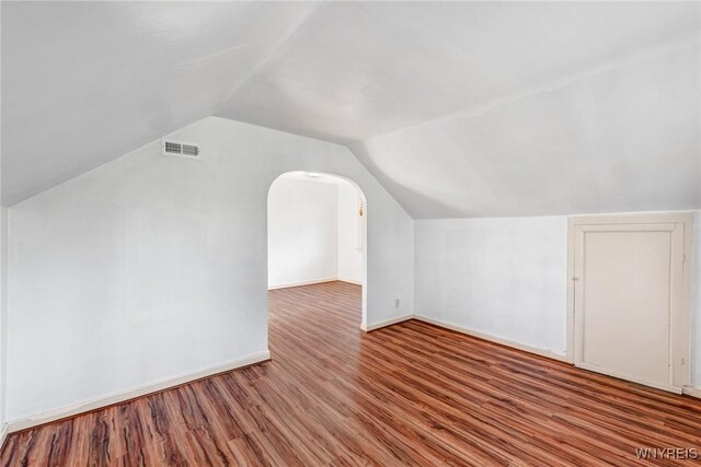 additional living space with vaulted ceiling, wood finished floors, baseboards, and arched walkways