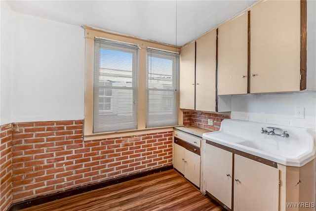 kitchen featuring light countertops, wood finished floors, brick wall, and backsplash