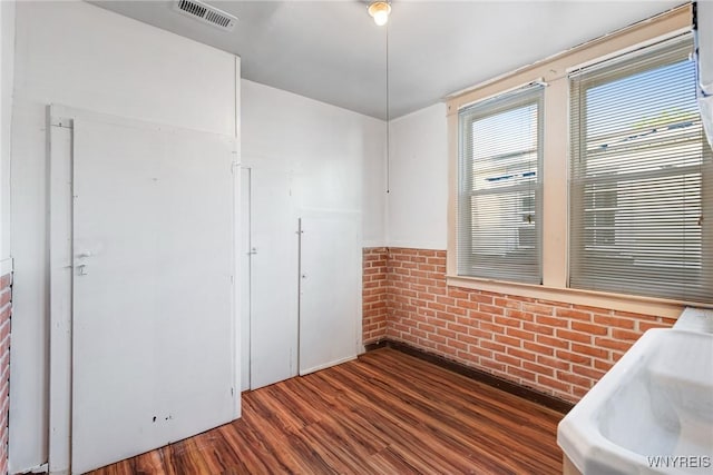 unfurnished room featuring brick wall and wood finished floors