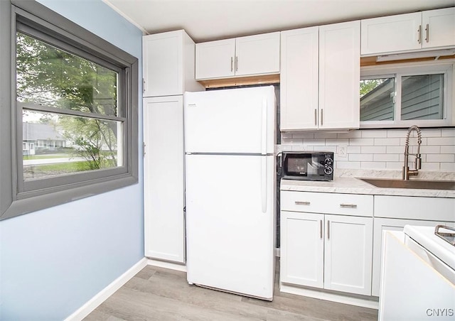 kitchen with freestanding refrigerator, a sink, light wood-style floors, and white cabinetry