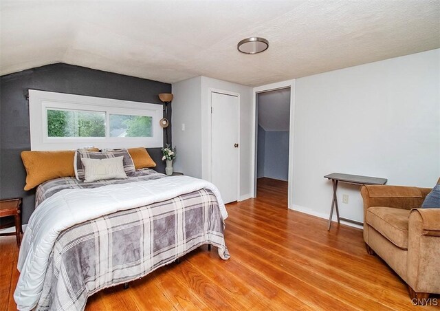 bedroom featuring light wood-style flooring, vaulted ceiling, and baseboards