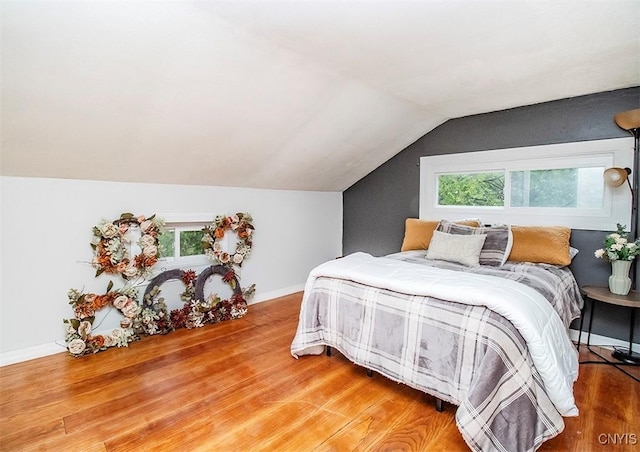 bedroom with wood finished floors, multiple windows, lofted ceiling, and baseboards