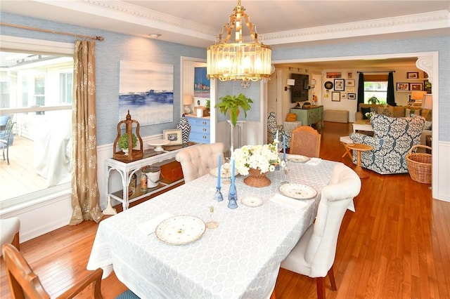 dining space featuring wallpapered walls, a chandelier, wood finished floors, and crown molding