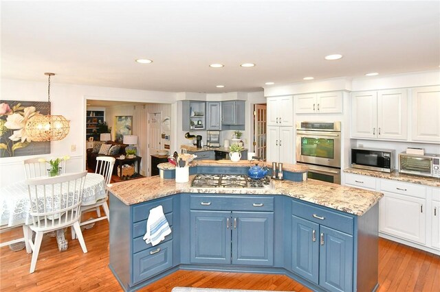 kitchen with stainless steel appliances, a center island, white cabinetry, light wood-style flooring, and light stone countertops