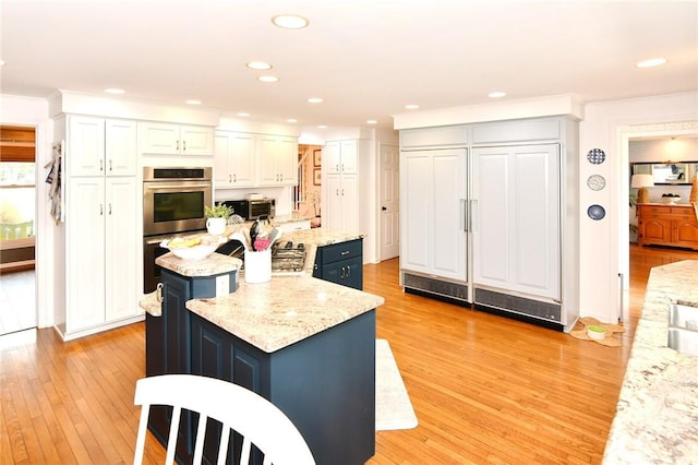 kitchen featuring stainless steel double oven, a kitchen island, white cabinets, light wood-type flooring, and recessed lighting