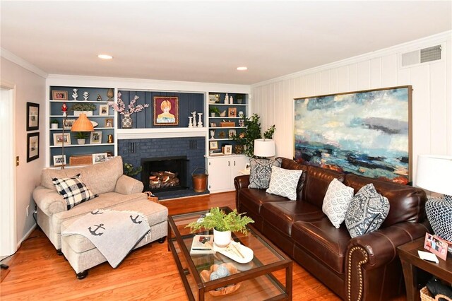 living room featuring ornamental molding, a brick fireplace, wood finished floors, and built in features