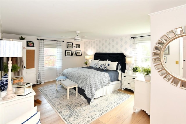 bedroom with wallpapered walls, light wood-style flooring, an accent wall, ceiling fan, and baseboards