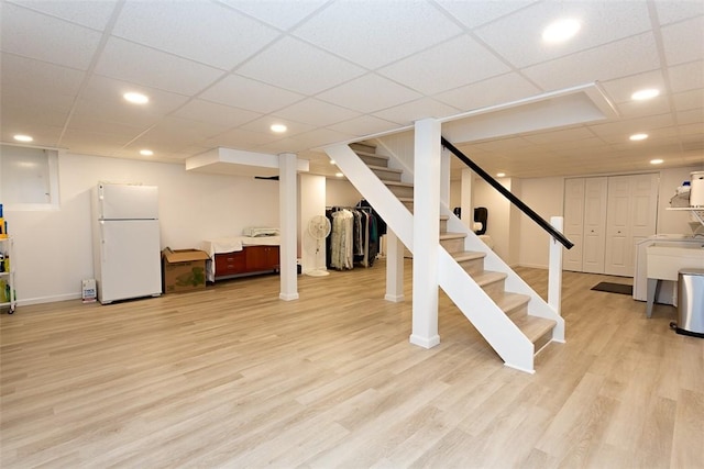 finished below grade area with freestanding refrigerator, stairway, light wood-type flooring, a paneled ceiling, and baseboards